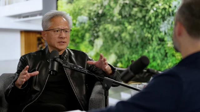 黄仁勋在《The Ezra Klein Show》录制现场,穿黑色皮夹克、面对主持人 Ezra Klein 说话