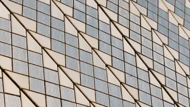 Close-up of the chevron-pattern ceramic tile cladding on the Sydney Opera House roof shells — alternating glossy white and matte cream tiles forming repeating geometric V-patterns