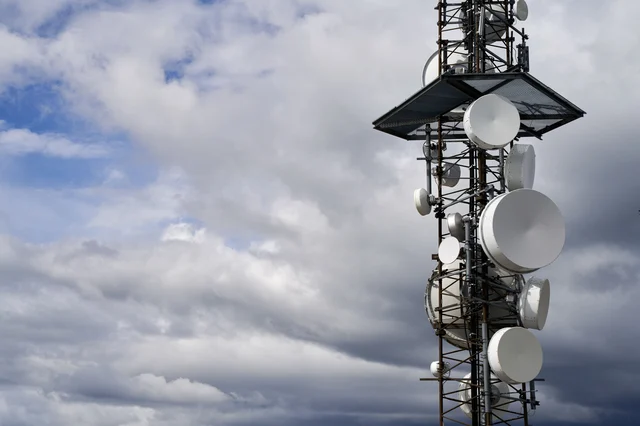 A telecommunications tower equipped with satellite dishes against a cloudy sky