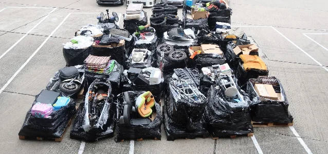 Large quantity of boxed goods — electronics, household items, and car parts wrapped in black plastic — laid out across a parking area after seizure from two ocean freight containers