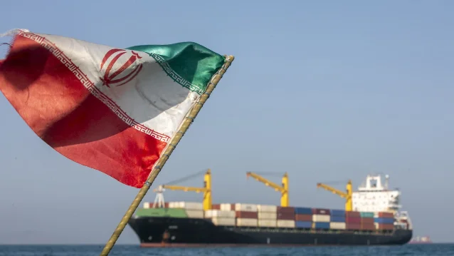 Iran flag flying over the Strait of Hormuz with a cargo vessel anchored in the background