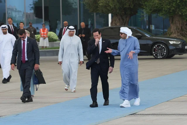 Secretary of State Marco Rubio walks alongside an Emirati official on a blue carpet in Abu Dhabi, accompanied by security personnel