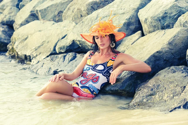 Woman in vibrant swimsuit relaxing by rocky shores