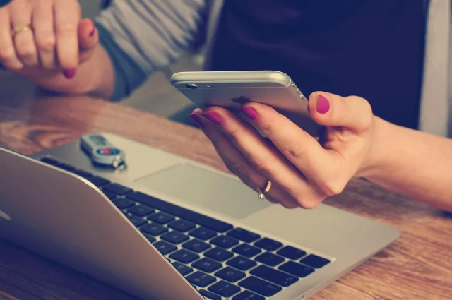 Person checking a phone next to a laptop