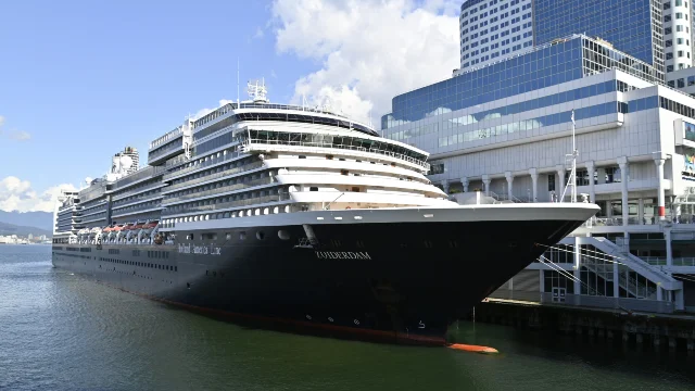 Holland America Line Zuiderdam cruise ship docked at a city port terminal, city skyline and mountains visible in the background