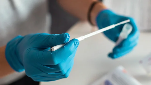 A woman in blue gloves prepares an HPV self-collection swab and sample container