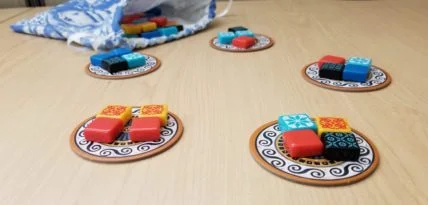 Azul 开局摆放的五个圆形工厂盘,各盘放置四块不同颜色的瓷砖,背景可见装砖用的抽绳布袋