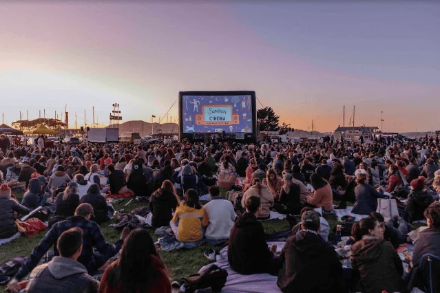 Large crowd on blankets watching the Sundown Cinema inflatable screen at an SF waterfront park at dusk