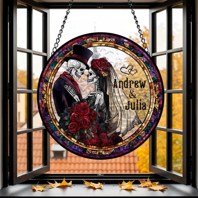 Round faux stained glass suncatcher showing a skeleton couple in formal wedding attire embracing, bride with floral headpiece and bouquet, groom in top hat, with names Andrew and Julia, warm orange-gold tones