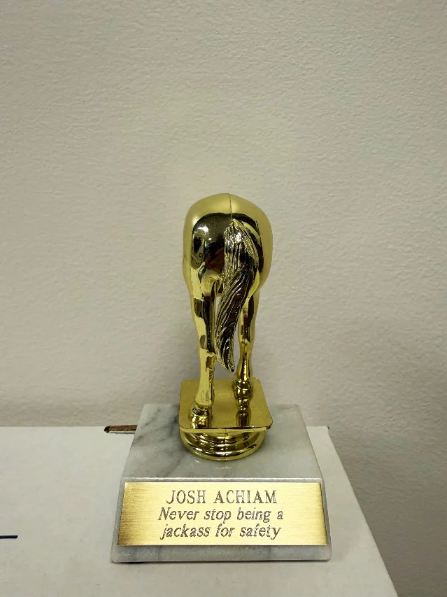 金色驴屁股奖杯,底座刻有「JOSHUA ACHIAM Never stop being a jackass for safety」