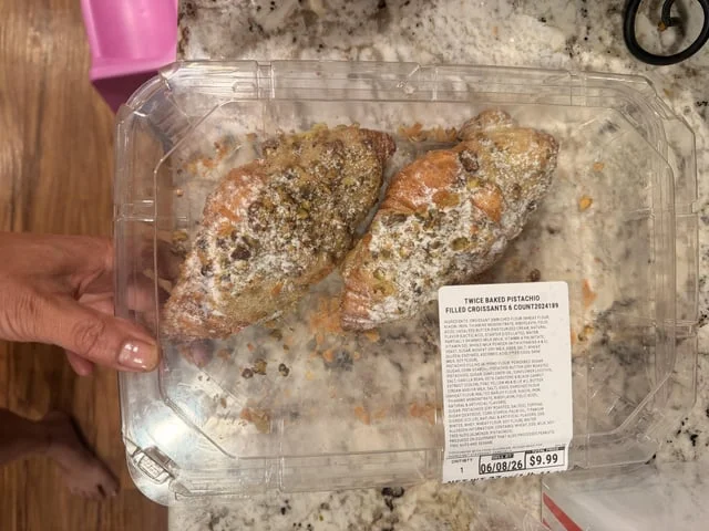 Kirkland Signature Twice-Baked Pistachio Filled Croissants stacked in Costco clamshells with powdered sugar and $9.99 price tag