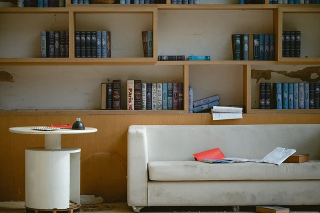 A vintage library reading room with bookshelves and papers scattered across a couch
