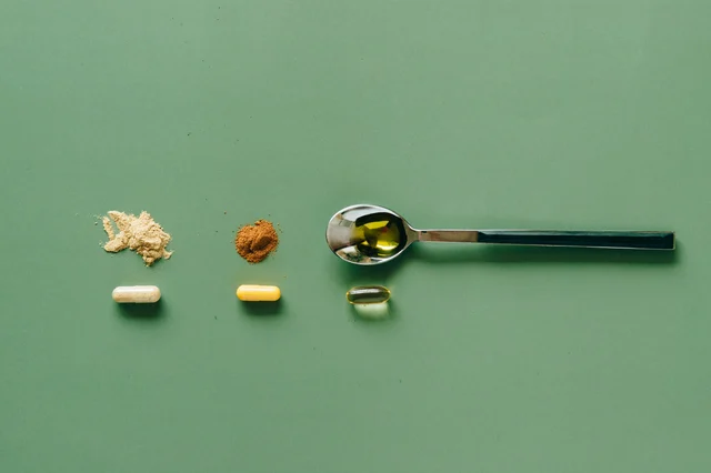 Assorted supplement powders and capsules in spoons on a green surface