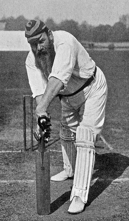 W.G. Grace in his batting stance, photographed circa 1878. The full-bearded Victorian cricketer leans over his bat in traditional whites.