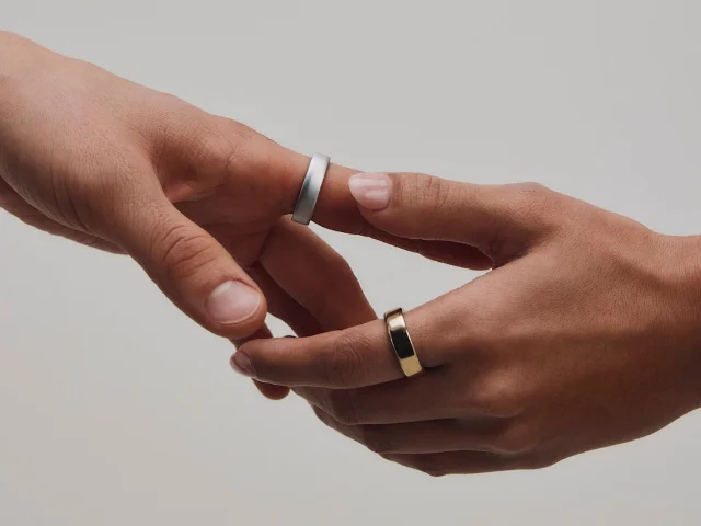 Two hands wearing Oura Ring 5 in silver and gold colorways, low-profile sensor surface visible