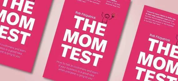 Three copies of The Mom Test book arranged in a fan, showing the hot pink cover design with stick figure holding lightbulb