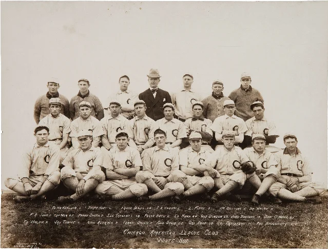 A sepia studio photograph of a baseball club in three staggered rows, the players in light flannel uniforms with a large C on the chest and a man in a dark suit and bow tie standing at the centre of the back row.