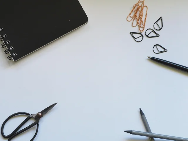 Notebook, clips, pens, and scissors on a white desk