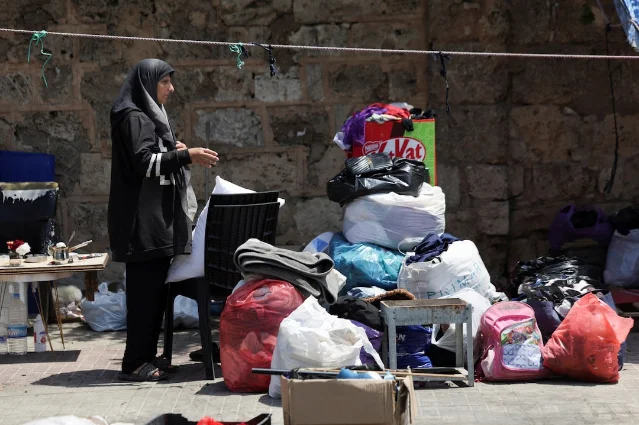 A displaced Lebanese woman stands beside her belongings in a Beirut street, preparing to return home after the US-Iran ceasefire took hold
