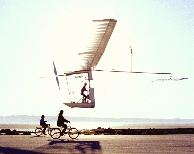 Gossamer Albatross II airborne at NASA Dryden, with two crew members on bicycles keeping pace directly below