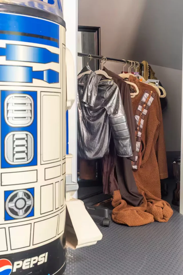 An R2-D2 Pepsi-branded cooler stands in the foreground; behind it, a closet rack holds a silver spacesuit, a Chewbacca costume, and other sci-fi dress-up pieces