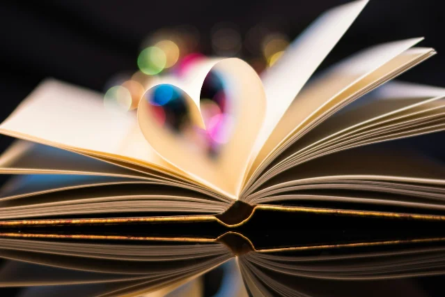 An open book with its pages folded into a heart shape — the visual shorthand for romantasy's central promise