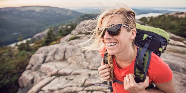 Hiker on the summit of Acadia NP's granite mountains, summer, with rolling forested hills and water in the distance