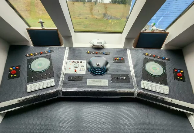The three-panel flight console — colored buttons, circular screen mounts, keyboards and instrument clusters under a panoramic skylight