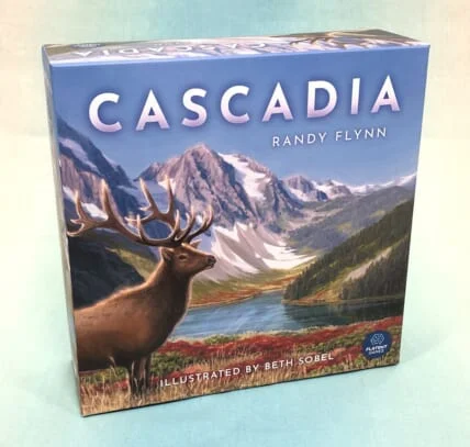 Cascadia 桌游包装盒实物,封面为山地湖泊景观,附有设计师和插画师署名