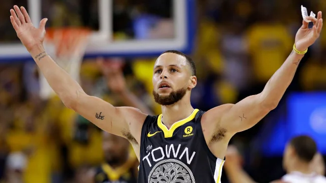 Curry raises both arms wide in his "The Town" Warriors jersey after draining a three in Game 2 of the 2018 NBA Finals