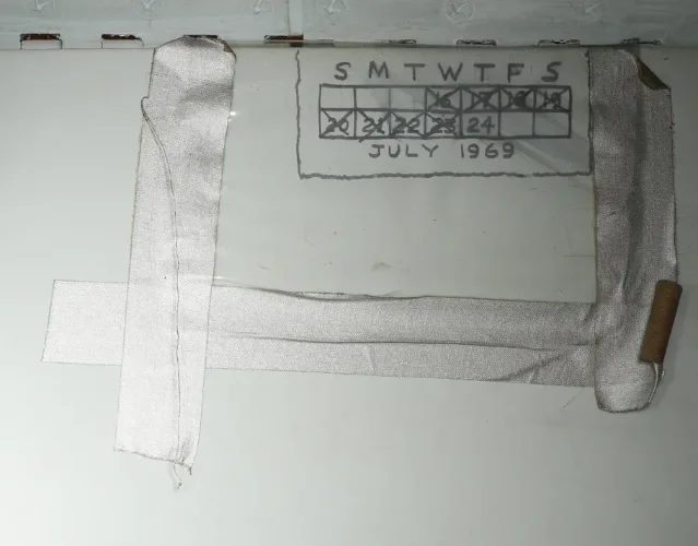 Hand-drawn mission calendar on a Columbia storage locker wall — July 1969, covered by translucent plastic sheet and duct tape; all days crossed off except splashdown day, July 24