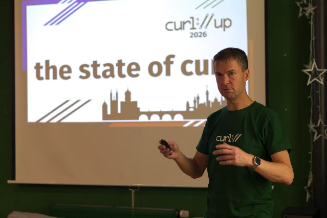 Daniel Stenberg presenting the "state of curl" keynote at curl up 2026 in Prague, wearing a green curl T-shirt