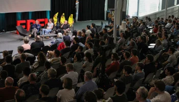 Full auditorium at EPFL Lausanne Ig Nobel Tour Show, with three performers in yellow banana costumes standing on stage behind seated presenters