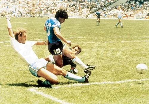 Maradona in Argentina's blue-and-white strip surging forward with the ball, two England defenders in white attempting sliding tackles as Azteca's packed stands fill the frame