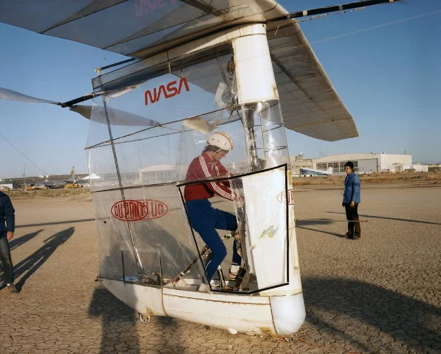 Pilot in the Gossamer Albatross cockpit at NASA Dryden, pedaling the bicycle-style drivetrain while a ground crew member stands nearby