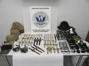 Seized counterfeit watches, eyeglasses, and headwear laid out on a table under a CBP Chicago Field Office sign — Port of Cincinnati