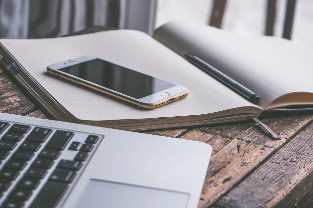 Phone resting on a notebook beside a laptop