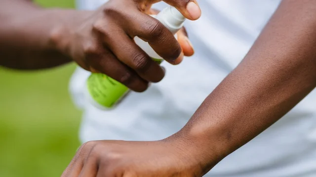 Person spraying insect repellent on their arm