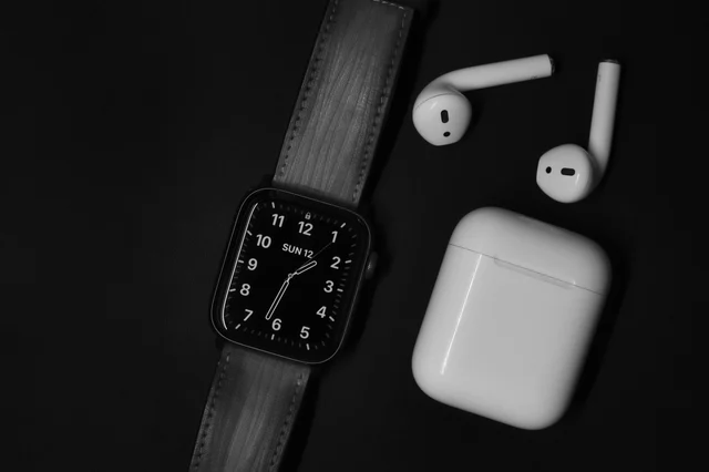 Black and white close-up of an Apple Watch and AirPods on a black surface