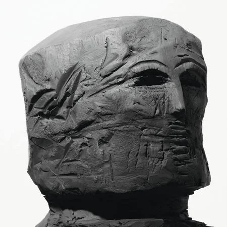 YHWH Nailgun Magazine album cover: close-up of a roughly carved grey wooden human head with visible chisel marks