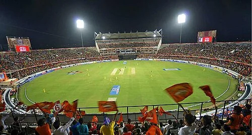 Aerial view of a packed IPL match at Hyderabad's Rajiv Gandhi International Cricket Stadium during the 2015 season, with orange flags waving in the stands under floodlights