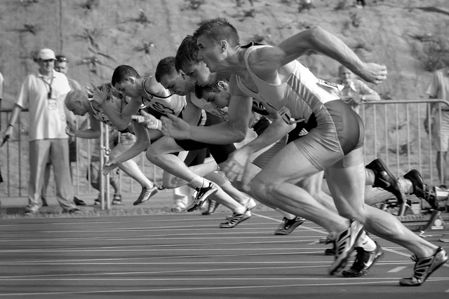 Sprinters burst from starting blocks in monochrome action photograph
