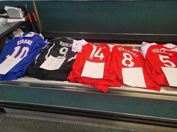 CBP inspection table at Newark Liberty showing a spread of seized counterfeit soccer jerseys, including Zidane, Ronaldo, Ødegaard and other player names visible on the backs
