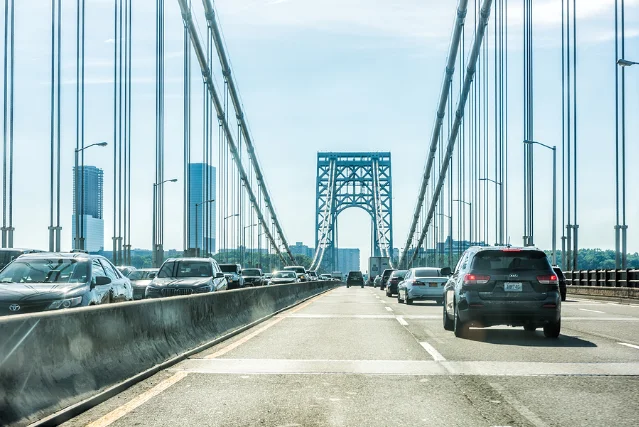 Bumper-to-bumper traffic on the George Washington Bridge, cars in multiple lanes, bridge tower in the background against a blue sky