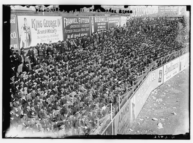 A packed crowd behind the outfield wall of the Polo Grounds, with painted advertising boards above the standing spectators