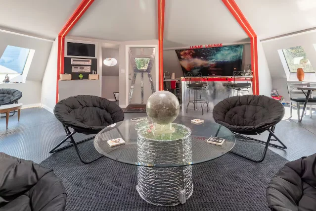 The Lunar Lounge interior — papasan chairs around a glass coffee table, red neon accent beams, a wet bar labeled "LUNAR LOUNGE" in the background
