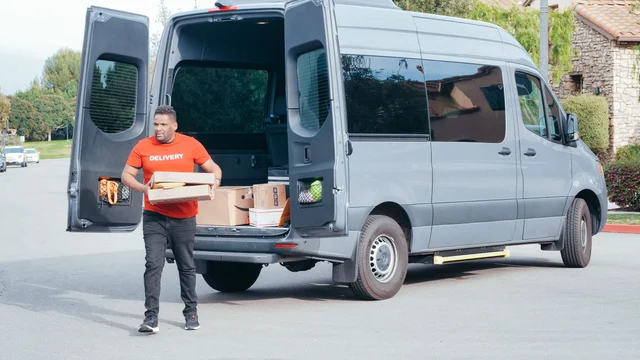 Operator unloading product from a van for a restocking run — route density determines whether this is a 2-hour day or an 8-hour one