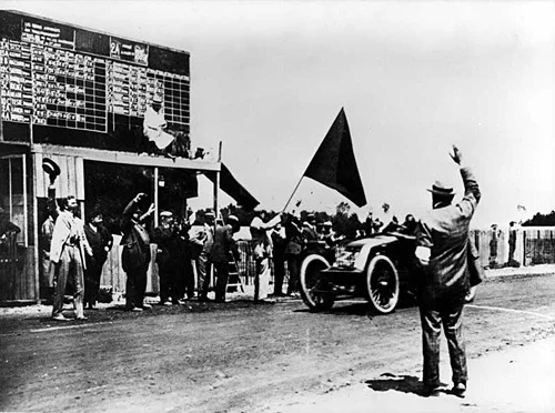 Szisz in his Renault AK 90CV crossing the finish line, surrounded by officials and spectators at the end of the 1906 Grand Prix