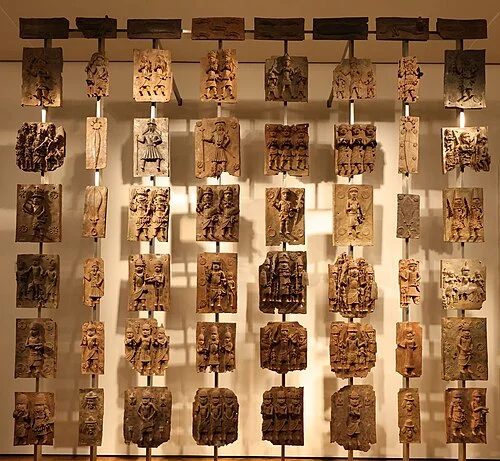 Benin bronzes on display at the British Museum in 2023, multiple plaques mounted on a white gallery wall