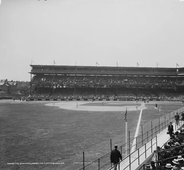 Forbes Field in Pittsburgh, seen from the right-field corner: a packed two-deck grandstand across the field, players at their positions, and spectators standing along the near fence